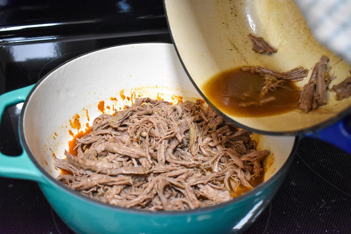 The shredded beef and broth being added to the pot with the sauce.