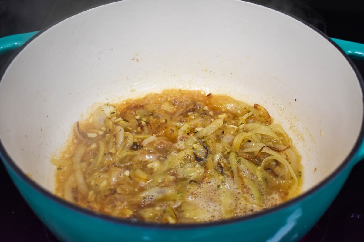 Onions, garlic, and spices after being deglazed with white wine in a light blue and white pot.