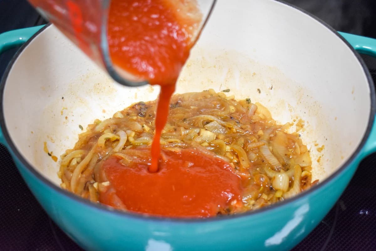 Tomato sauce being added to the ingredients in the pot.