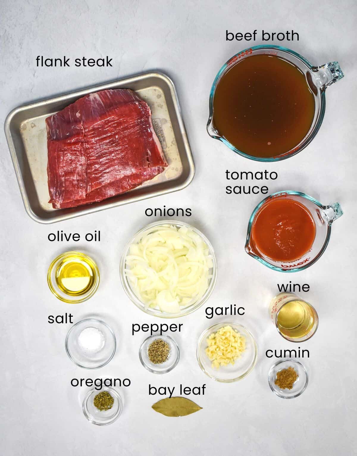 The ingredients for the dish arranged on a white table with each one labeled with black letters.