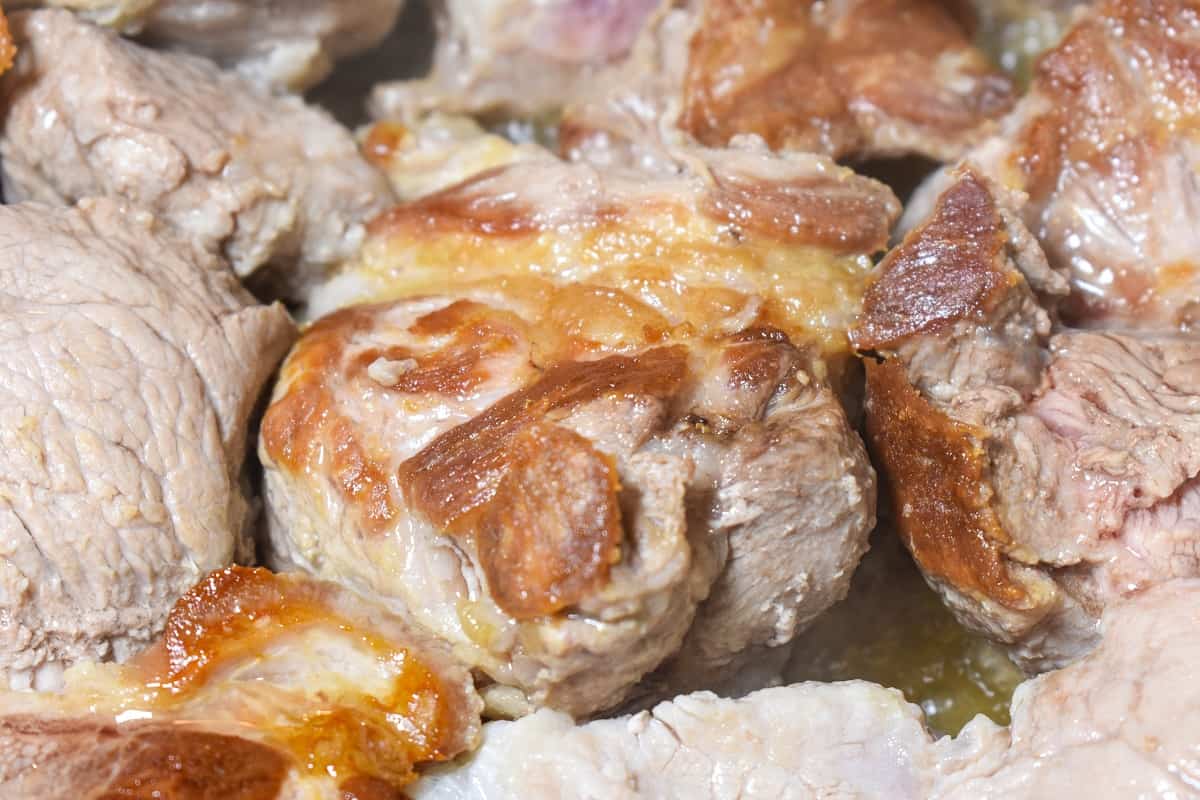 A close up image of large pork chucks browning in a pot.