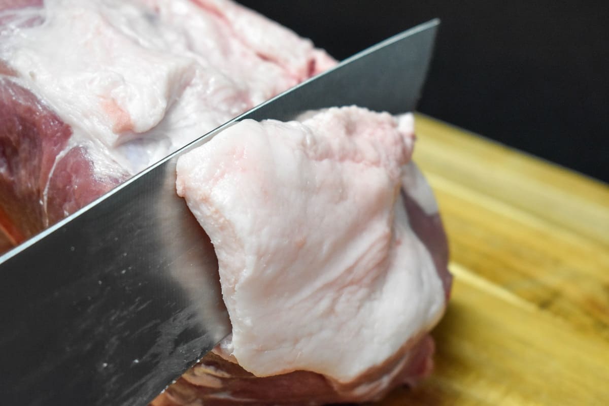 A large knife cutting fat off a pork shoulder.