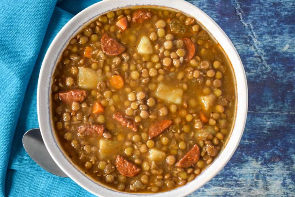 The lentil soup served in a white bowl and displayed on a blue table with an aqua colored linen.