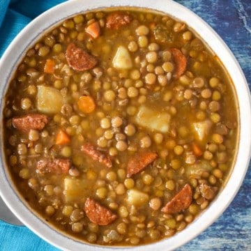 The lentil soup served in a white bowl and displayed on a blue table with an aqua colored linen.