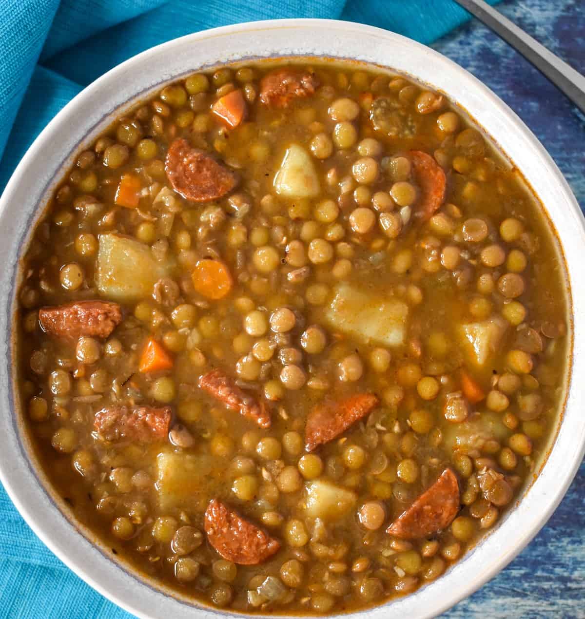 A close up image of lentil chorizo soup served in a white bowl.