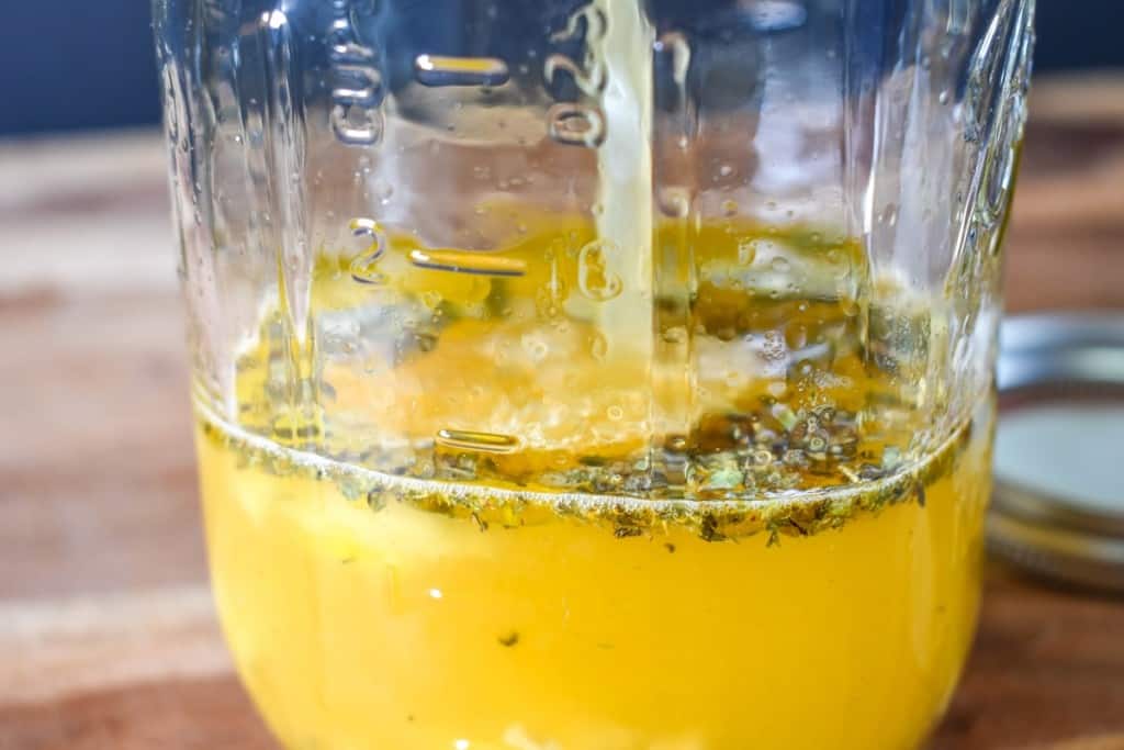 Sour orange juice being added to a jar with spices and the garlic in it already.