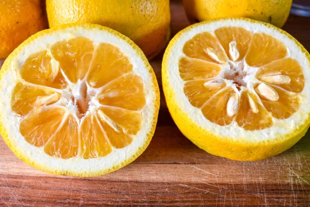 A sour orange cut in half so the inside is exposed. It is set on a wood cutting board.