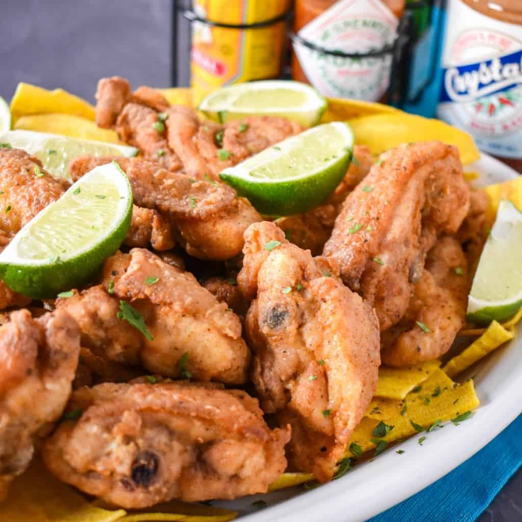 Chicharrones de pollo on a bed of plantain chips garnished with lime wedges.
