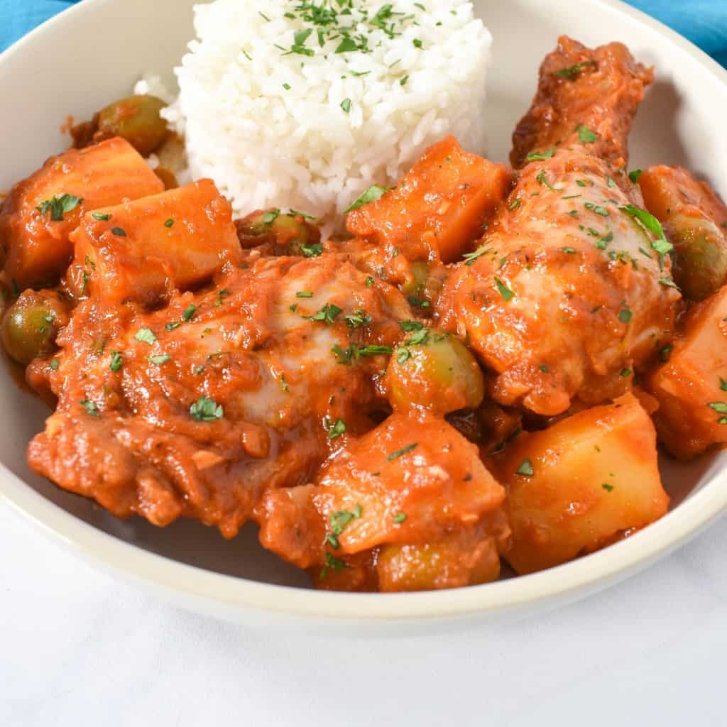 A close up image of the fricase de pollo (chicken fricassee) served with a side of white rice in a white plate and garnished with chopped parsley.