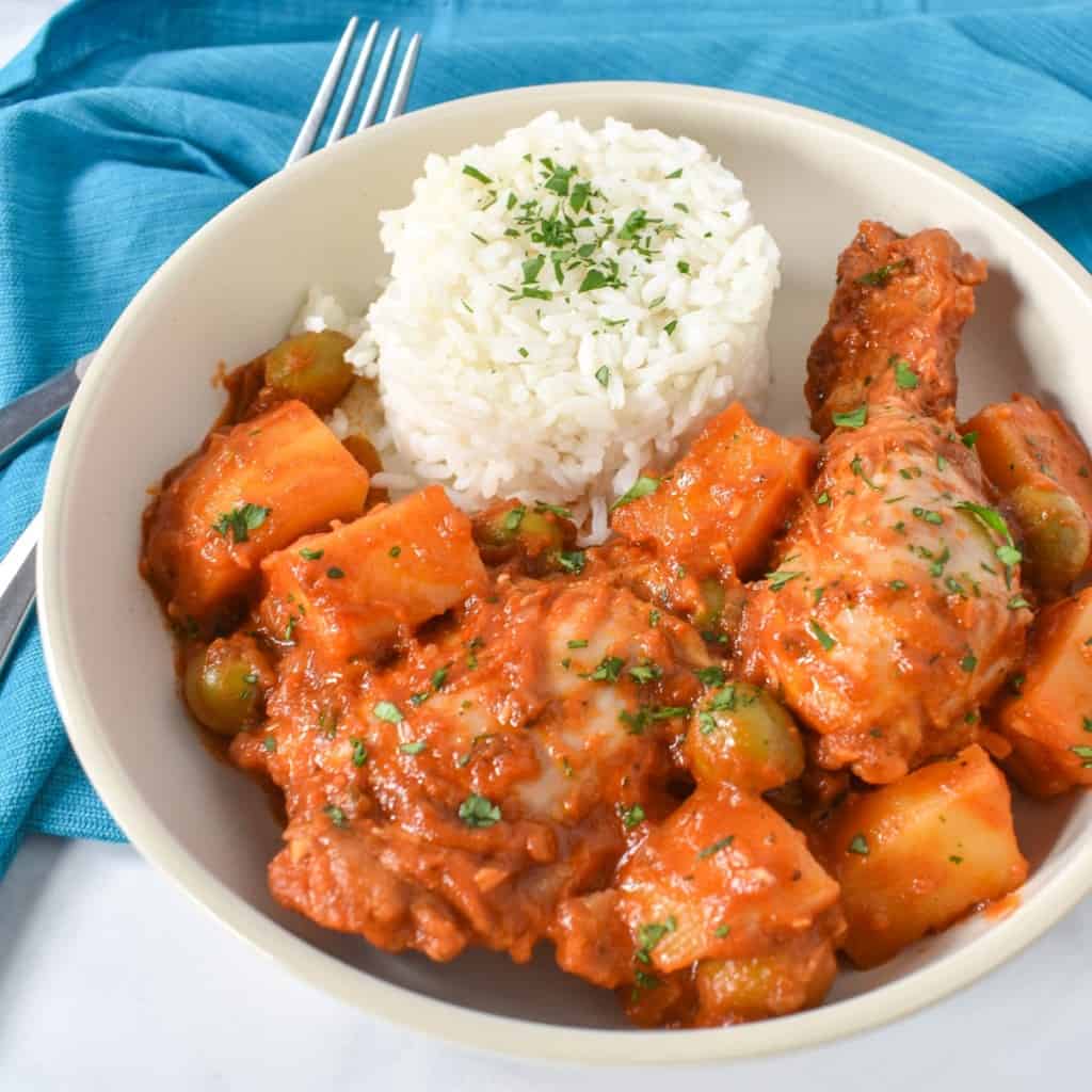 The chicken fricassee served with white rice and garnished with parsley in a white plate with an aqua linen.