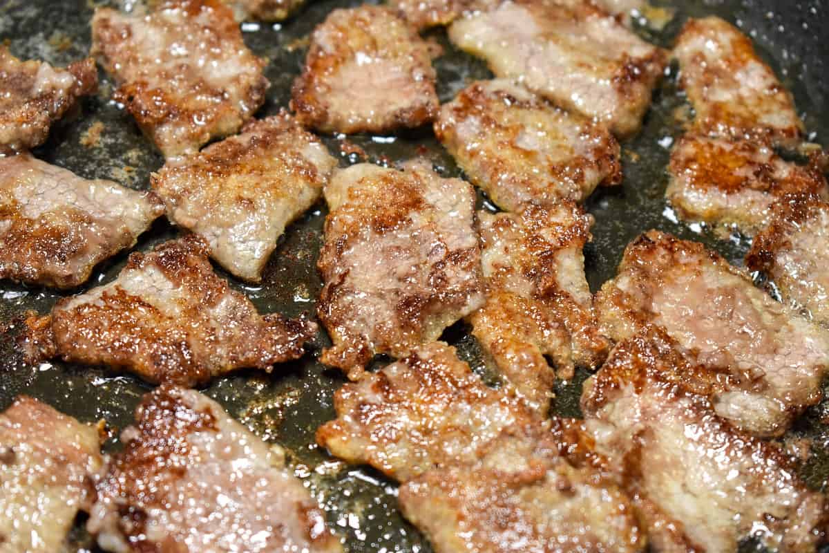 Beef slices that have been cooked until golden-brown in a black non-stick skillet.