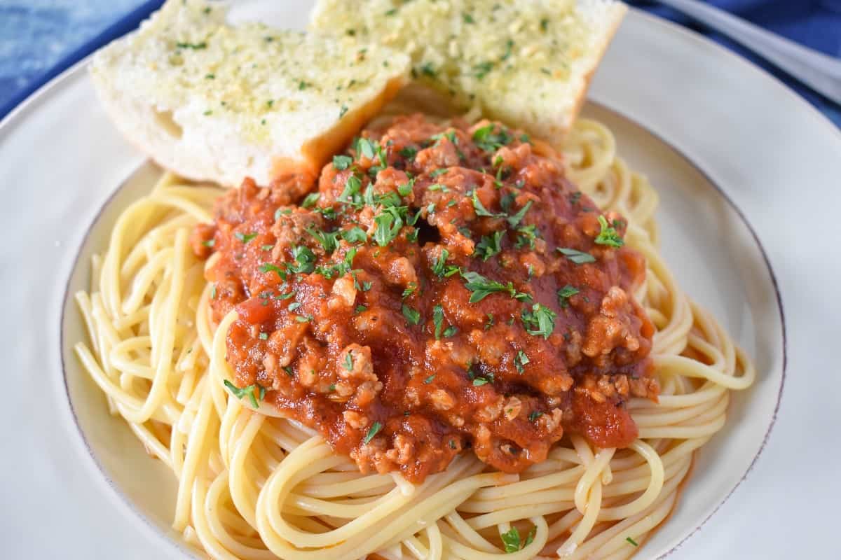 The Italian sausage spaghetti served on a white plate with garlic bread.
