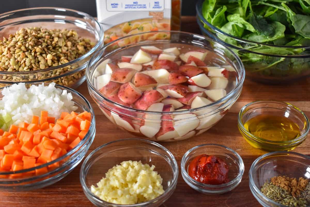 The prepped ingredients for the soup arranged in glass bowls on a wood cutting board.