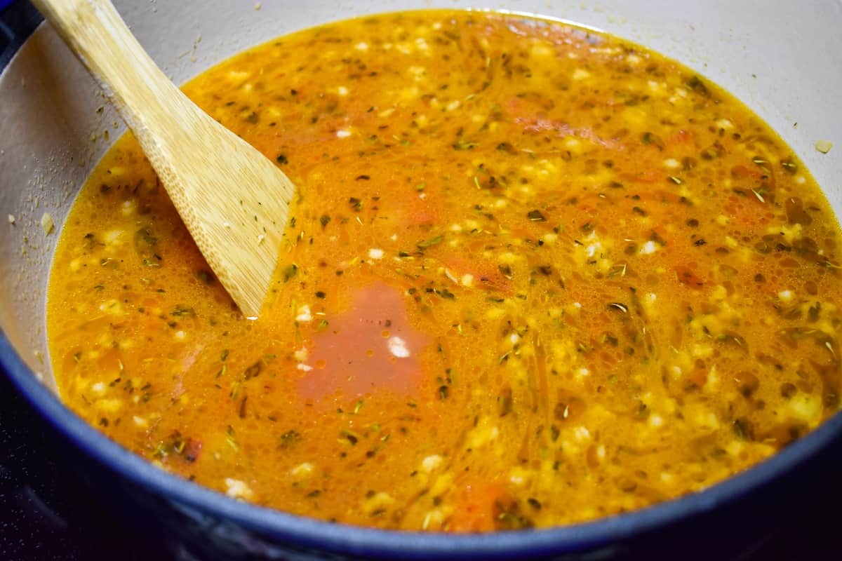 An image of the broth with the vegetables in a large blue pot with with interior.