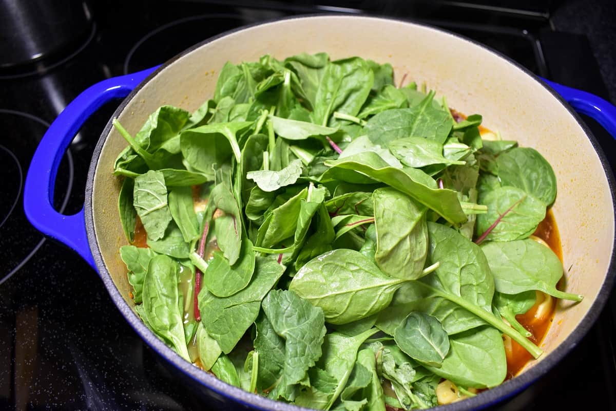 Leafy greens covering the top of the broth in a large blue pot with a white interior.