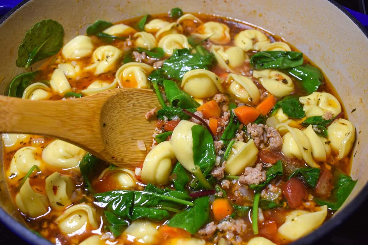 The soup being stirred with a wood spoon now with the greens wilted and significantly reduced in volume.