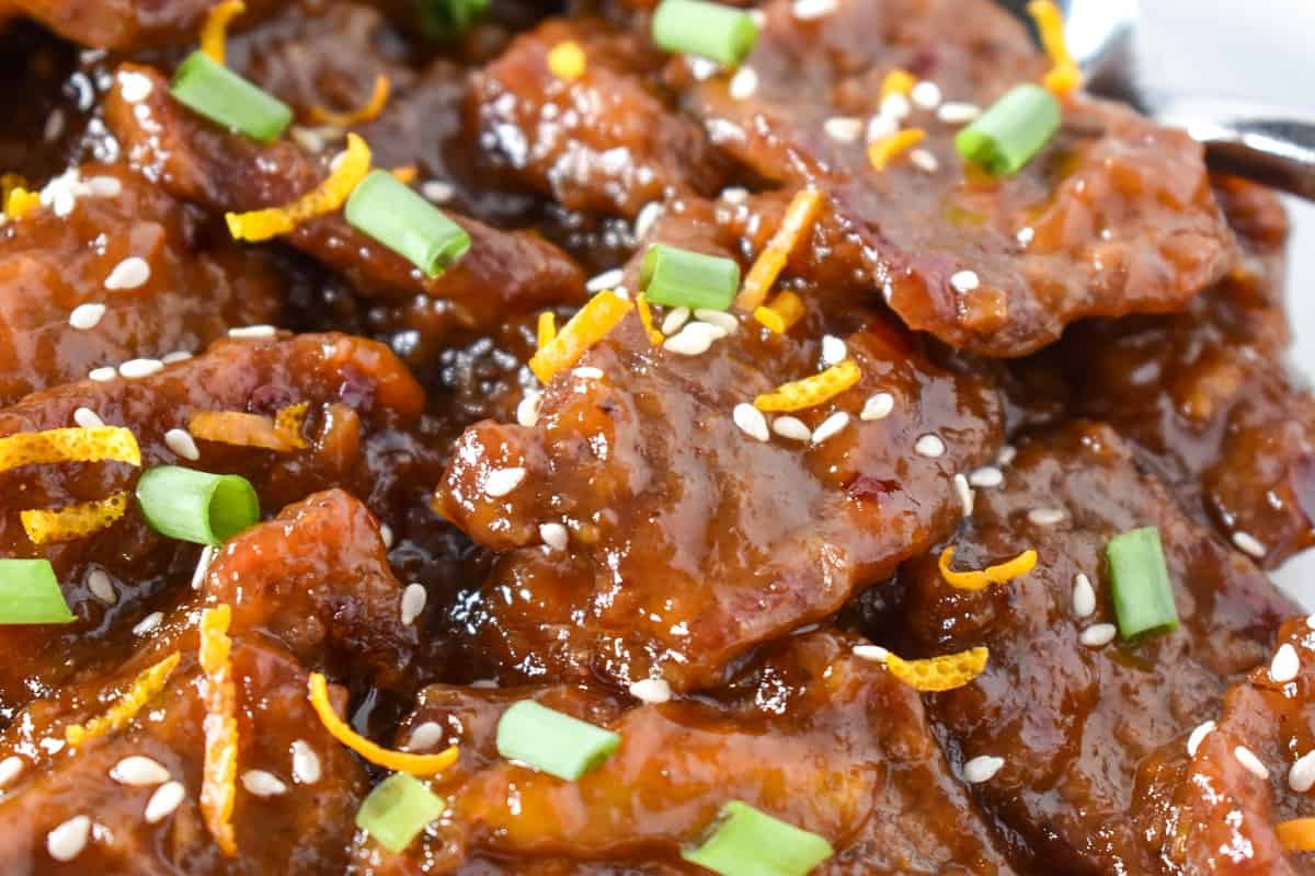 A close up image of the orange beef garnished with orange zest, sesame seeds and sliced green onions.