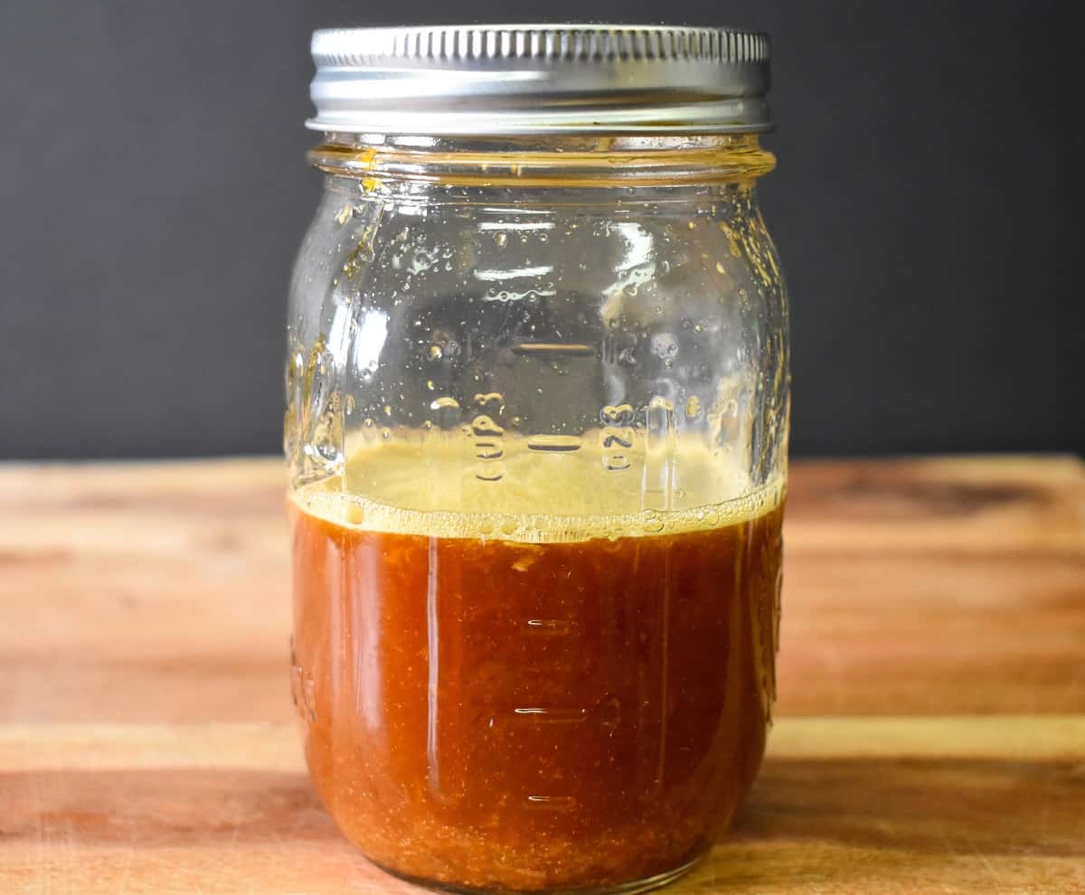 The orange sauce, which is a reddish-brown color in a canning jar displayed on a wood cutting board.