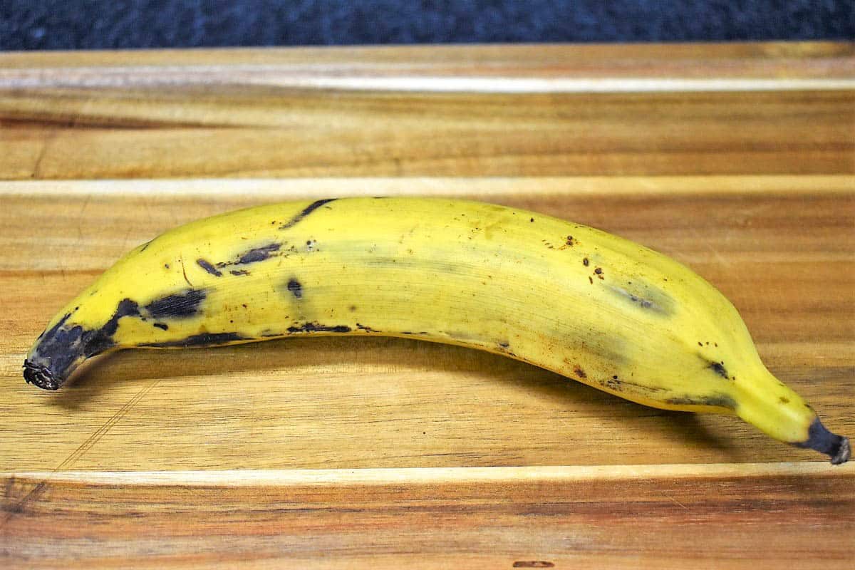 A semi-ripe plantain on a wood cutting board.