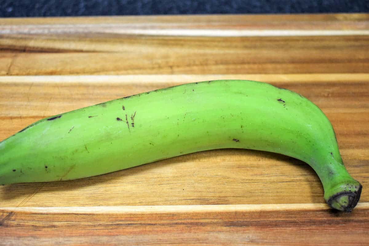 Un plátano verde sobre una tabla de cortar de madera
