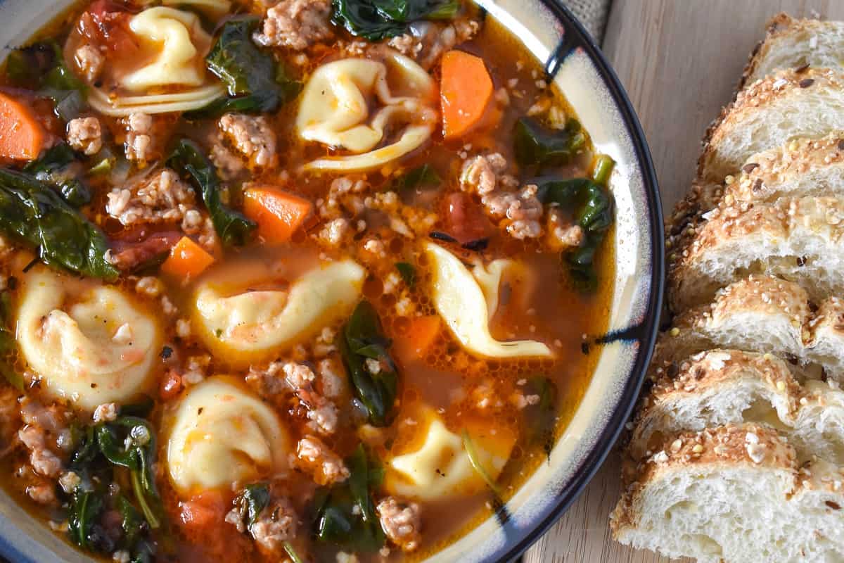 A close up of the soup with tortellini, sliced carrots, small pieces of sausage, and small tomato pieces floating on the surface.