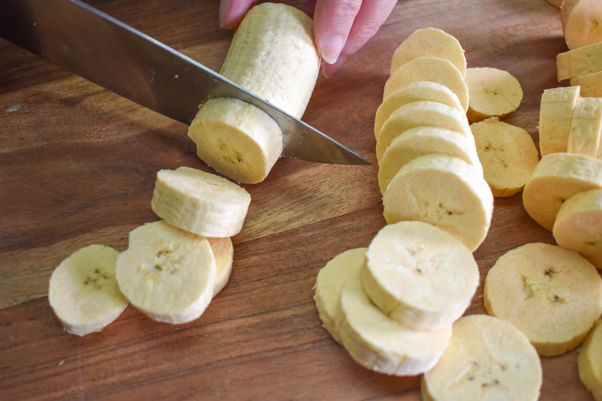 Slicing Green Plantains on a wood cutting board.