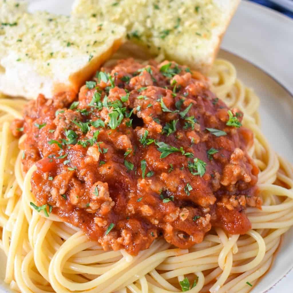 Spaghetti served on a white plate topped with sausage tomato sauce and garnished with parsley.