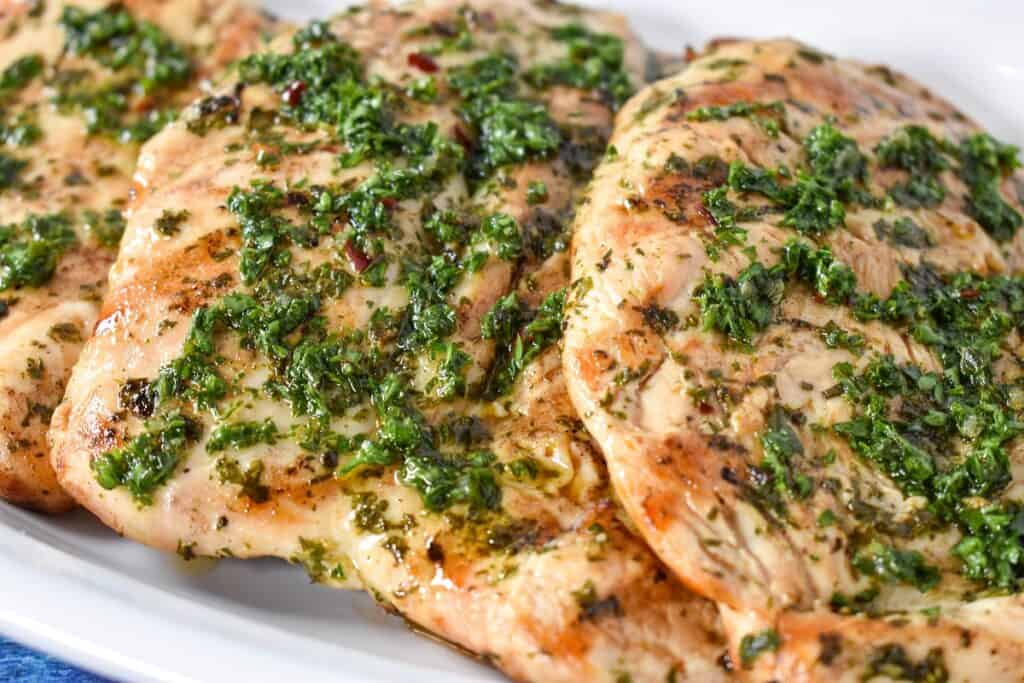 Grilled Chicken topped with chimichurri sauce served on a white platter.