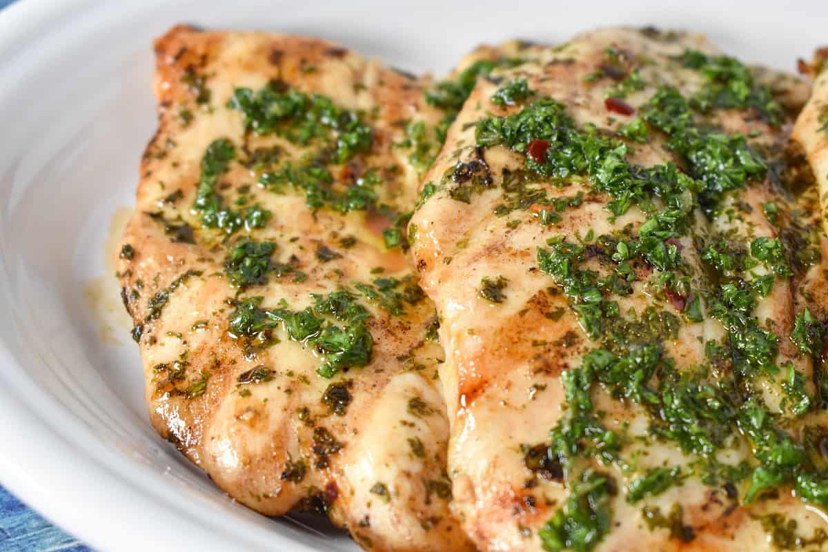 A close up image of the grilled chicken with the sauce served on a white platter.