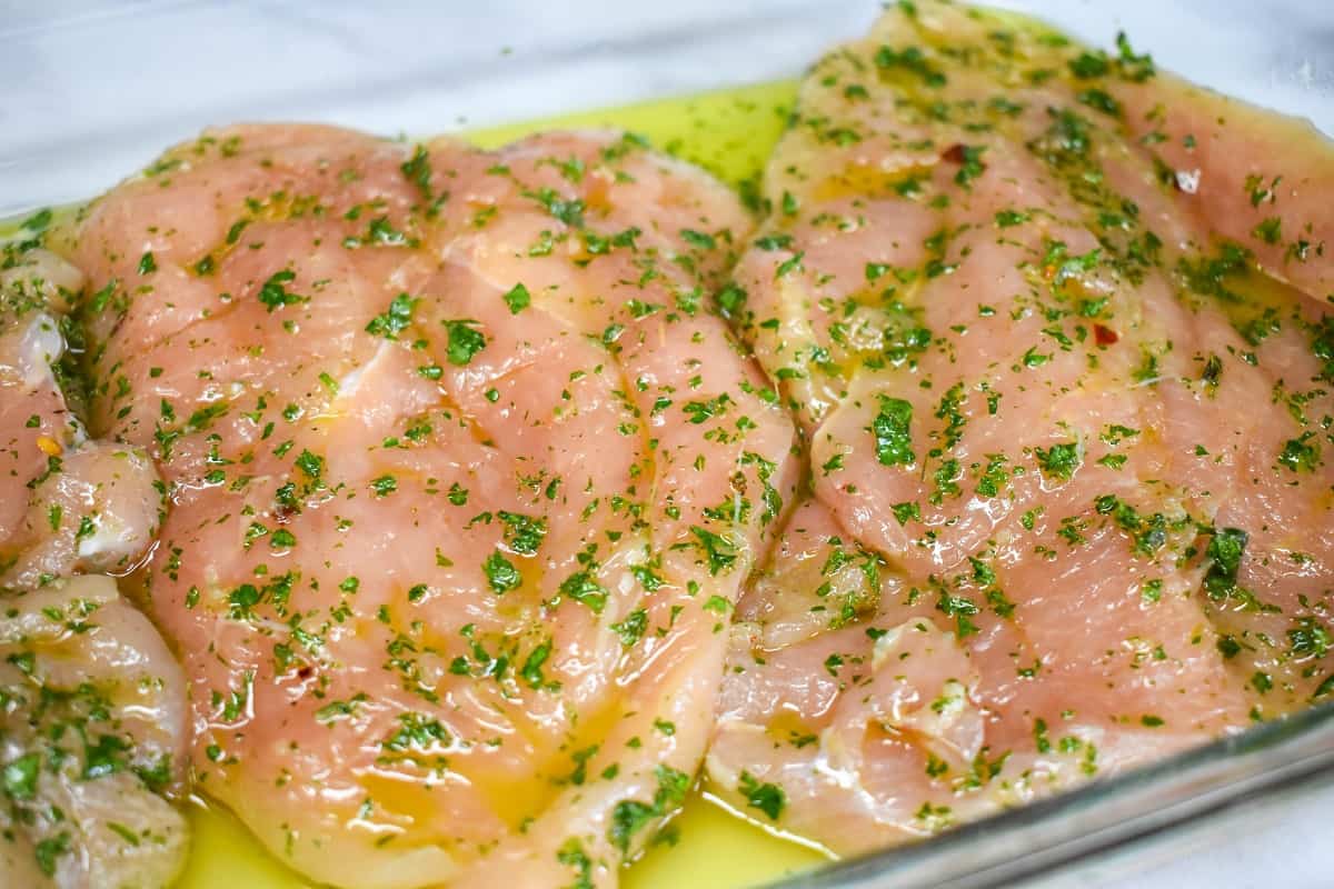 Chicken breasts marinating in chimichurri in a glass pan.