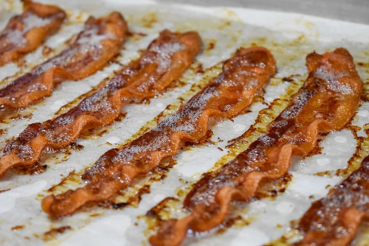 Cooked, crispy bacon slices arranged on a large baking sheet that's lined with white parchment paper.