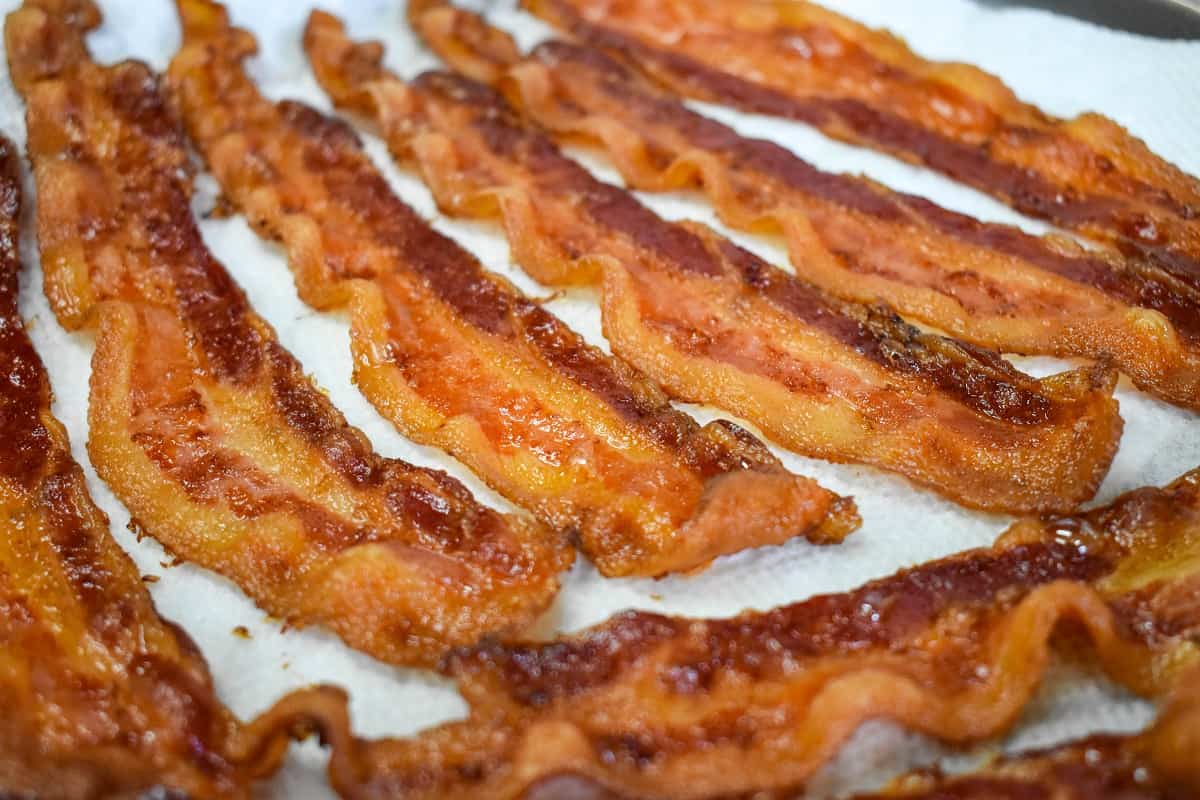 The cooked bacon slices draining on a white paper towel.