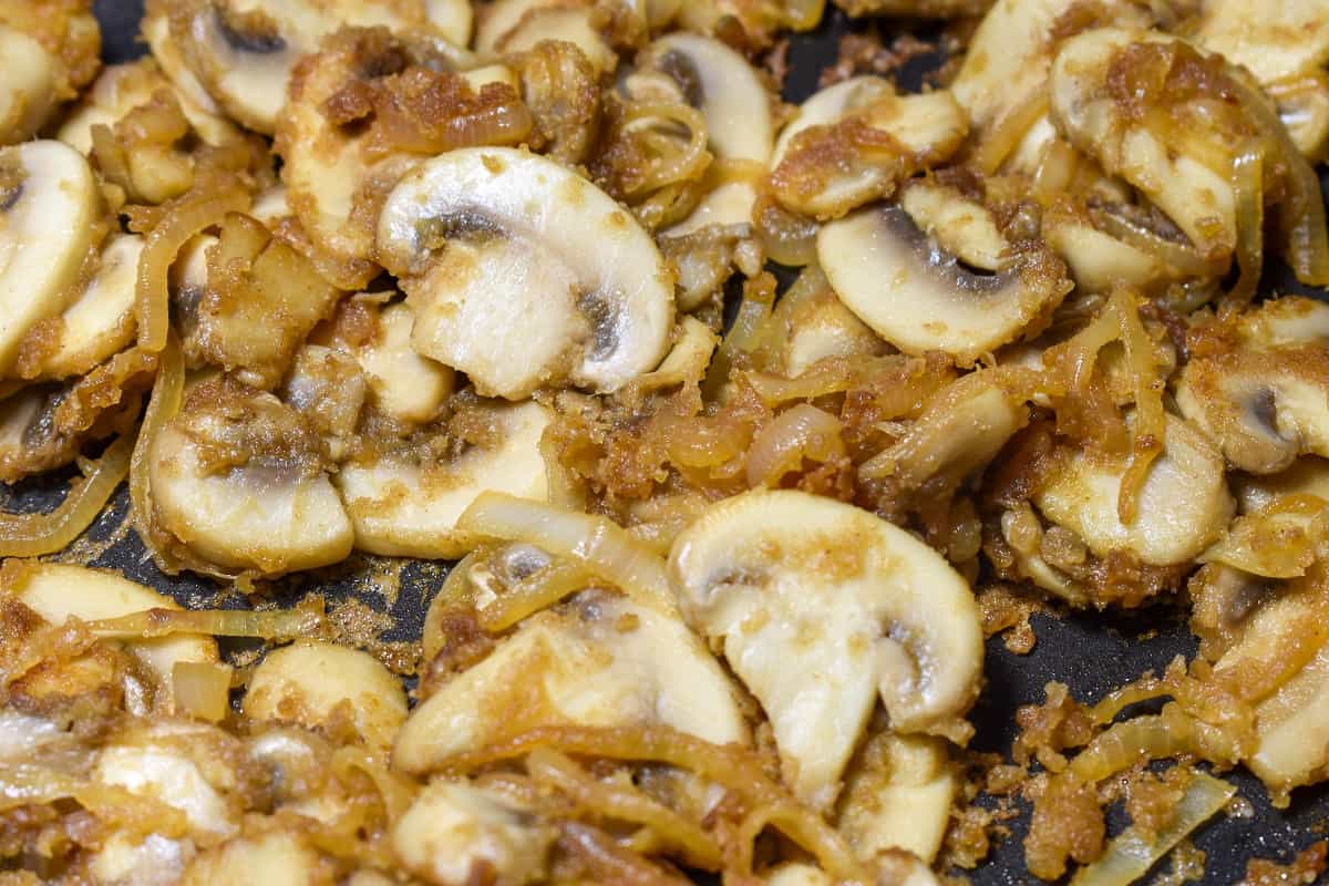 A close up image of the sliced onion, mushroom and flour mixture cooking in a black skillet.