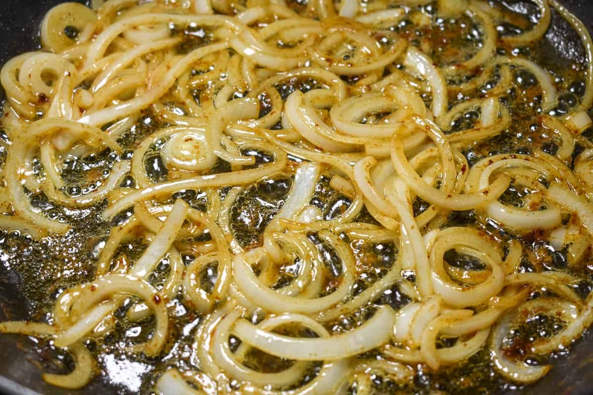 A close up image of thin sliced onions cooking gently in butter.