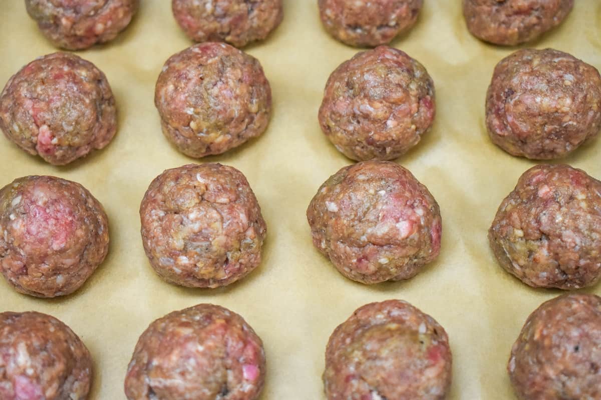 Formed meatballs arranged in four rows on a sheet pan lined with parchment paper.