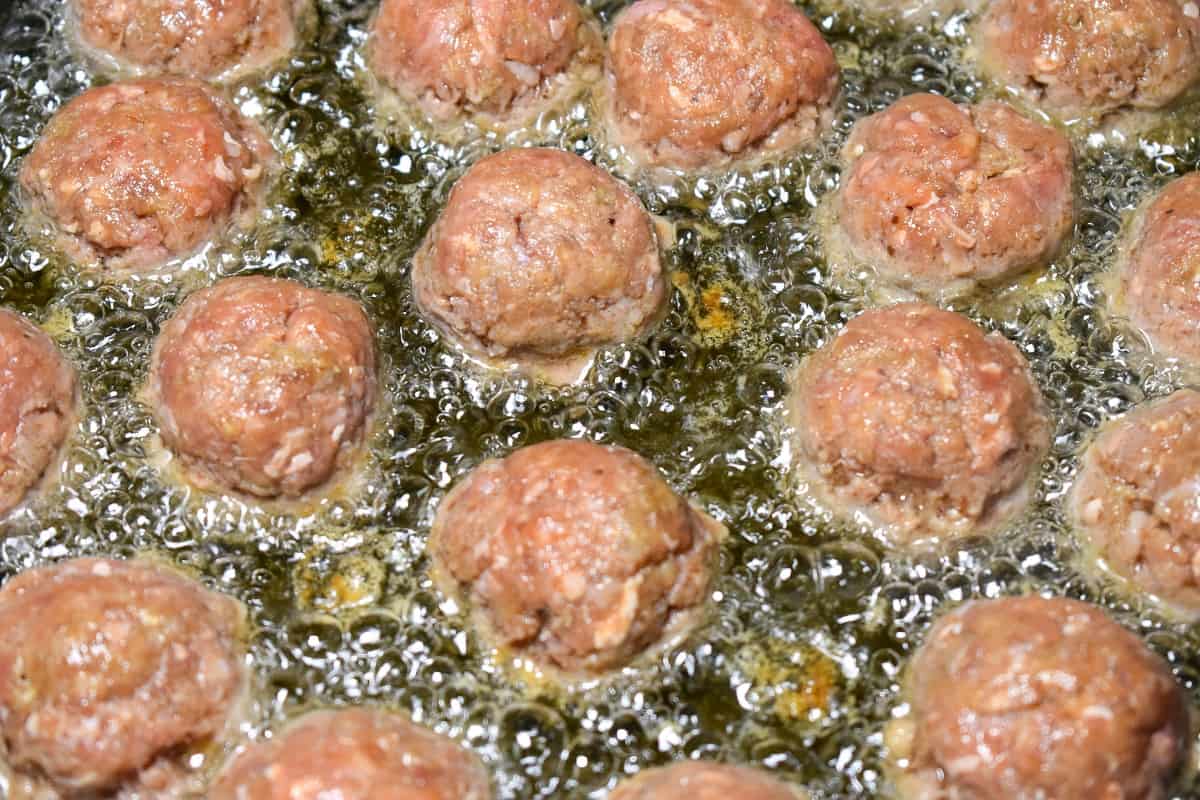 A close up of meatballs frying in oil. The oil is covering about half the meatball.