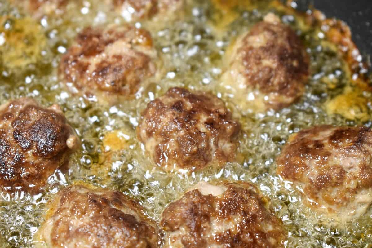 A close up of meatballs frying in oil and the top part is browned already. The oil is covering about half the meatball.