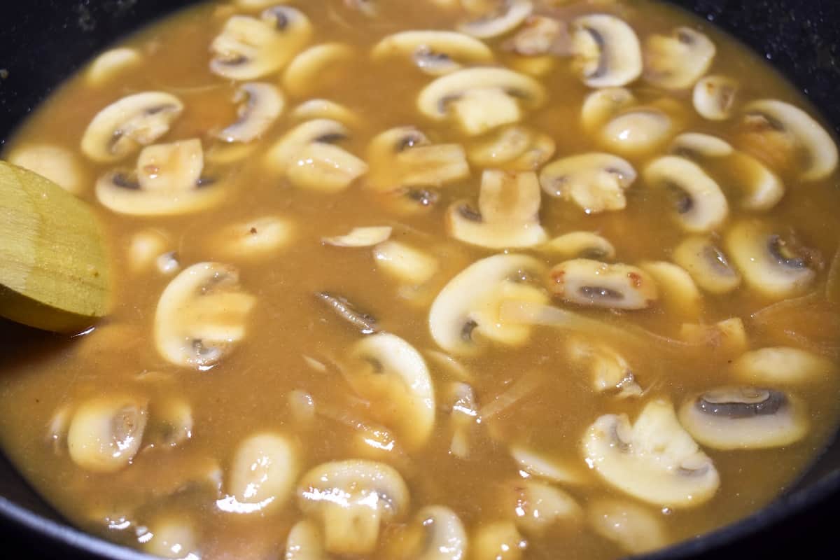 Sliced mushrooms, onions and beef broth in a large, black skillet.