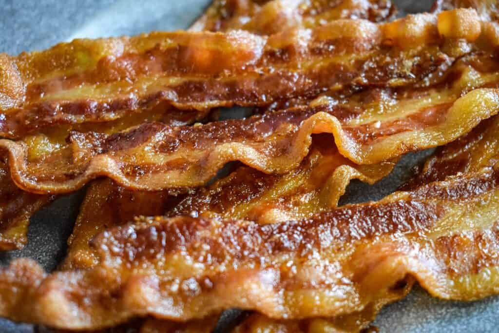 A close up image of a few slices of cooked bacon on a gray plate.