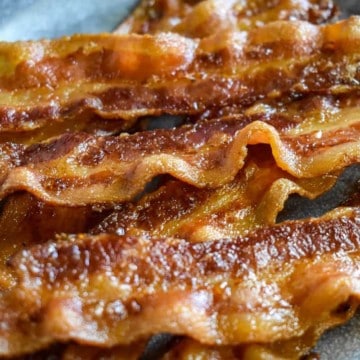 A close up image of a few slices of cooked bacon on a gray plate.