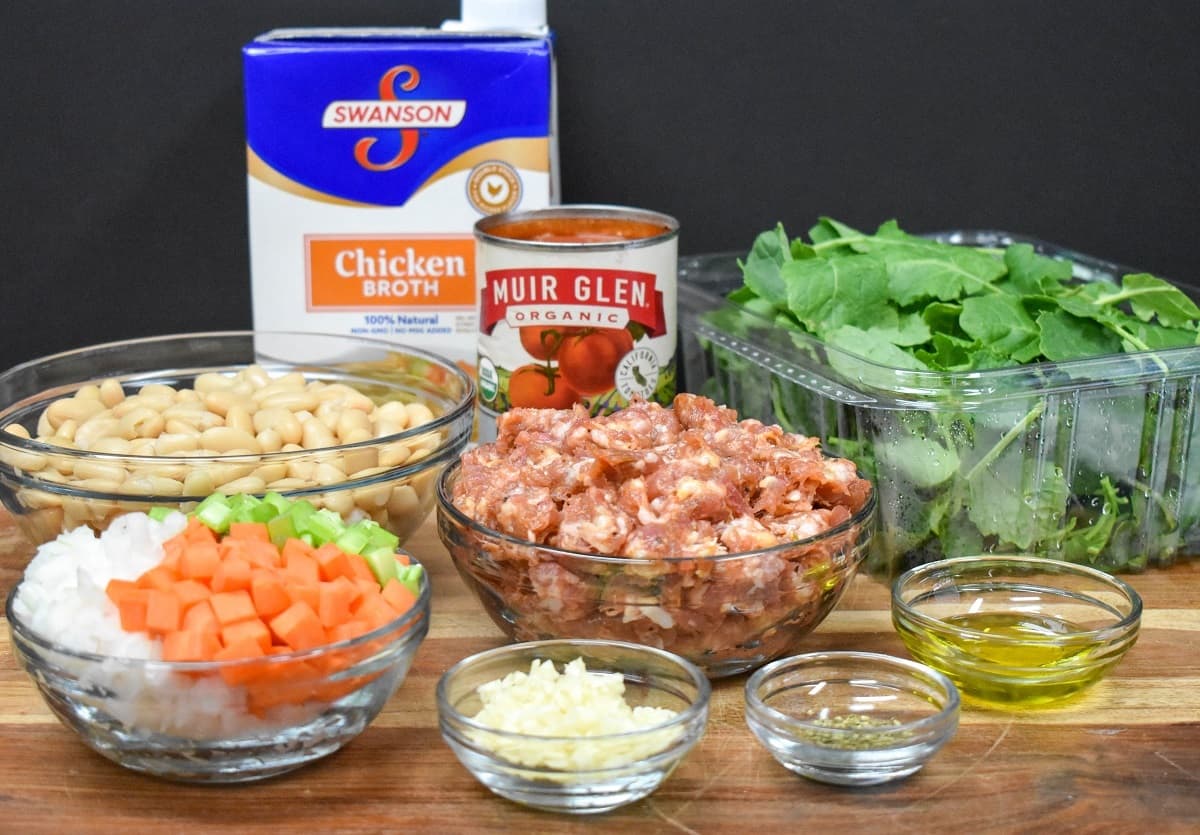 The ingredients for the soup, prepped and separated in glass bowls and displayed on a wood cutting board.