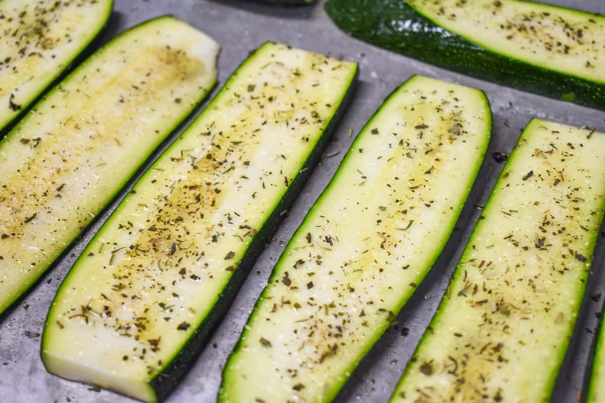 Seasoned zucchini slices before cooking arranged on a baking sheet.