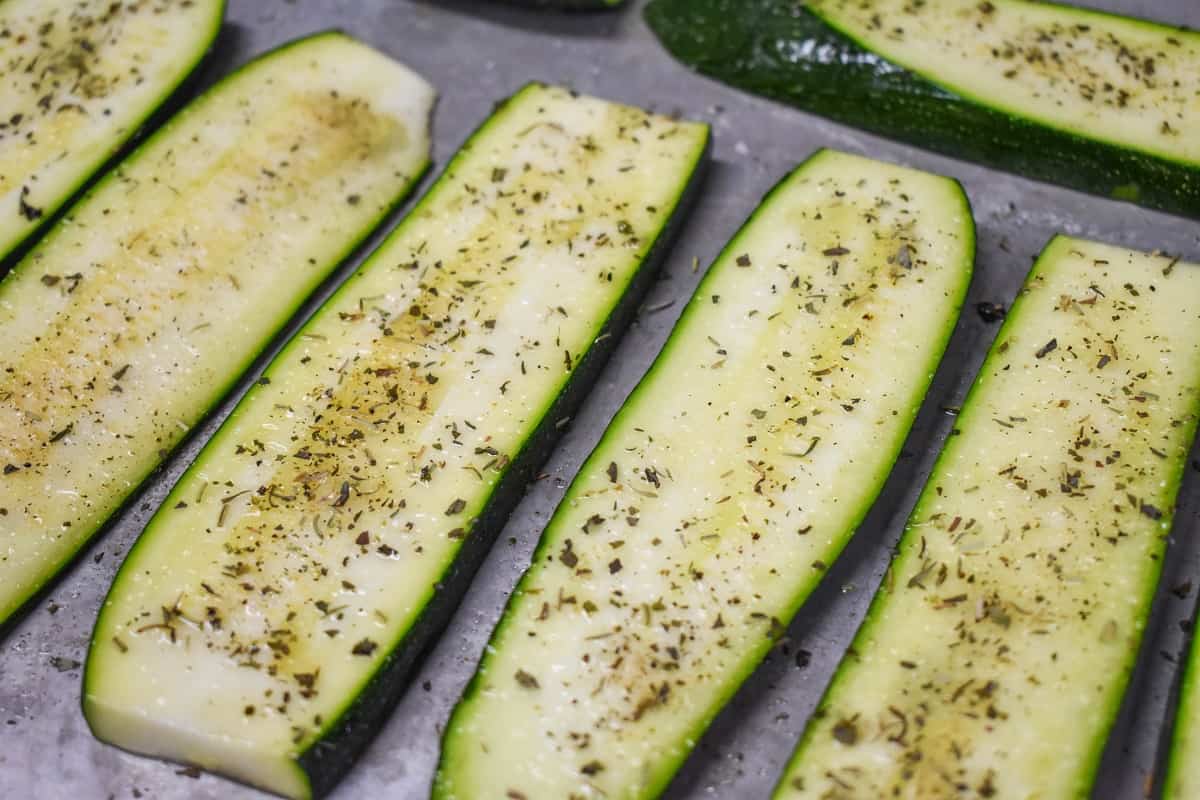 Seasoned sliced zucchini arranged on a metal baking sheet.