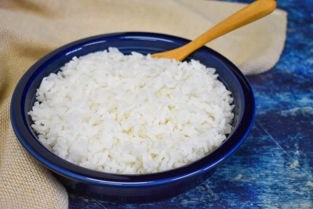 White rice served in a blue bowl displayed with a beige linen and a wooden spoon on a blue table.