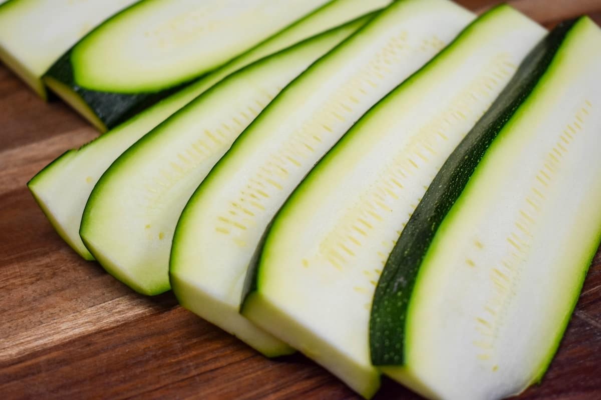 Sliced, uncooked zucchini fanned out on a wood cutting board.