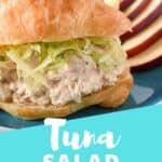 Tuna salad on a croissant topped with shredded lettuce with sliced apples and celery on the side and an aqua blue graphic that reads tuna salad sandwich. The graphic is used for Pinterest.