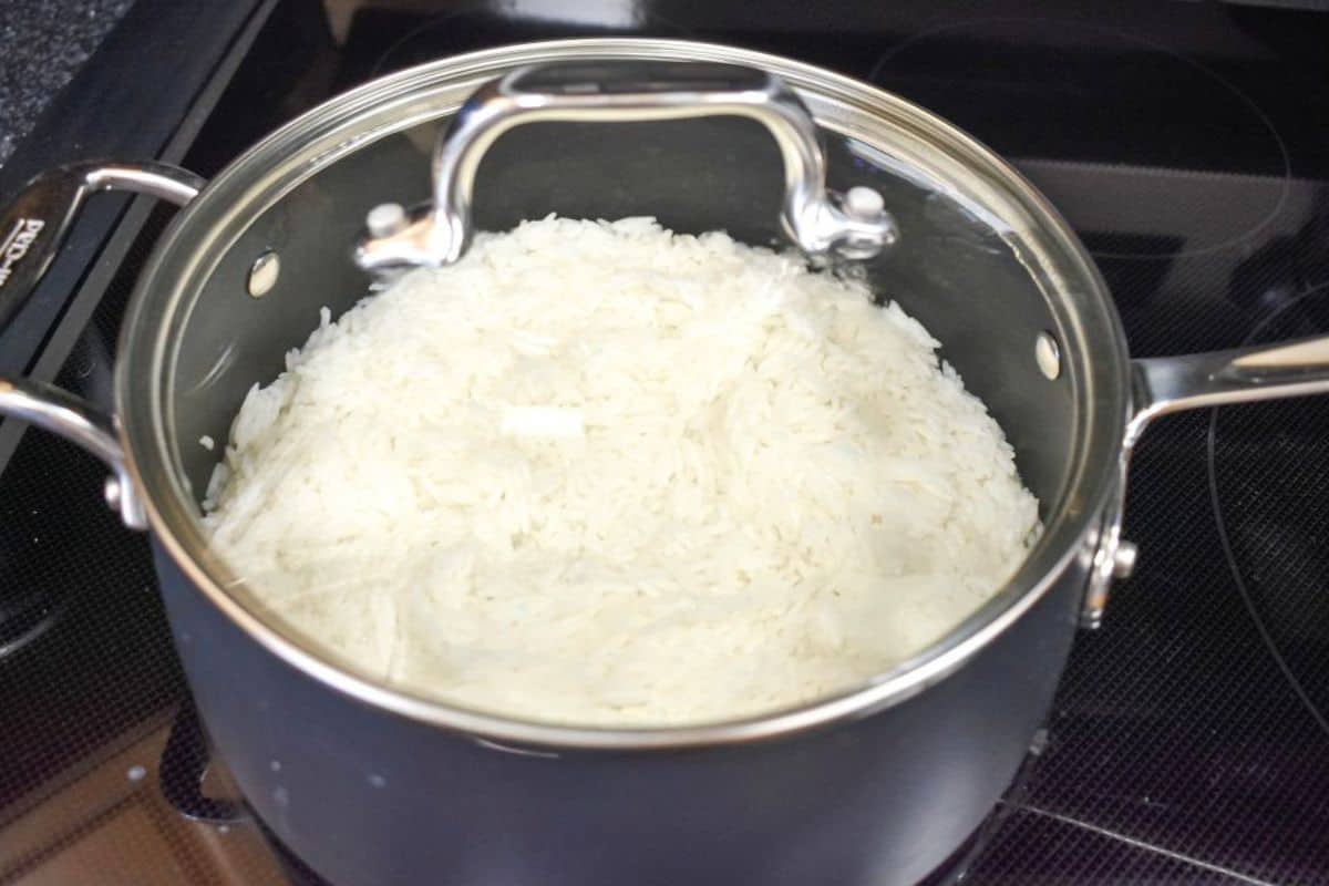Rice cooking, covered, in a black saucepan with a glass lid.