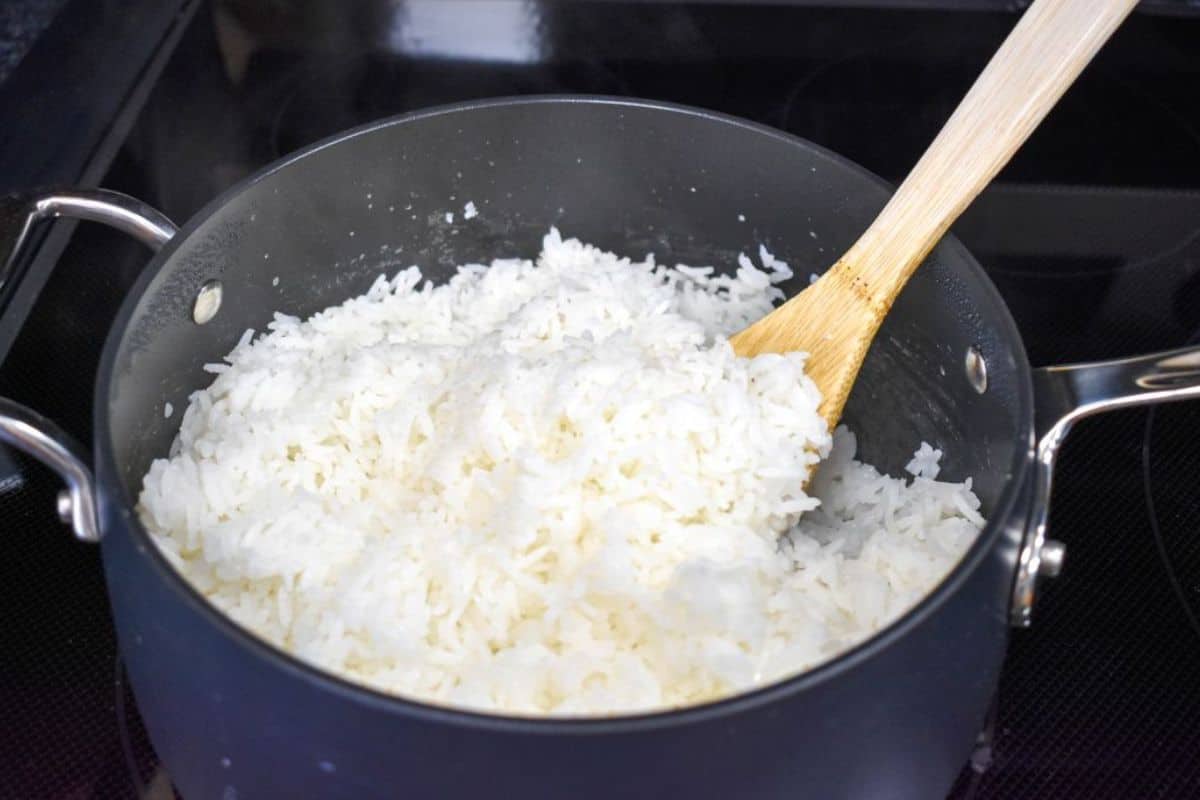 White rice being stirred with a wood spoon, in a black saucepan.
