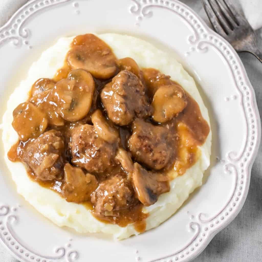 An image of the meatballs and mushroom gravy on a bed of mashed potatoes served on a white plate.