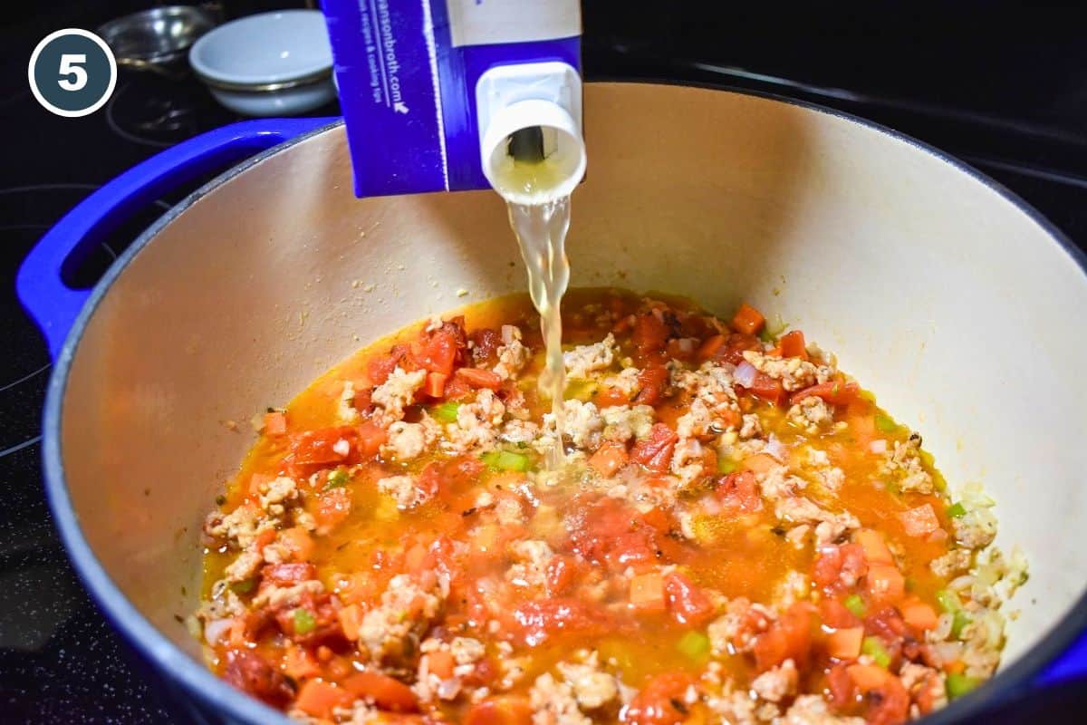 Chicken broth being poured into the pot with the sausage, tomatoes, and vegetables.